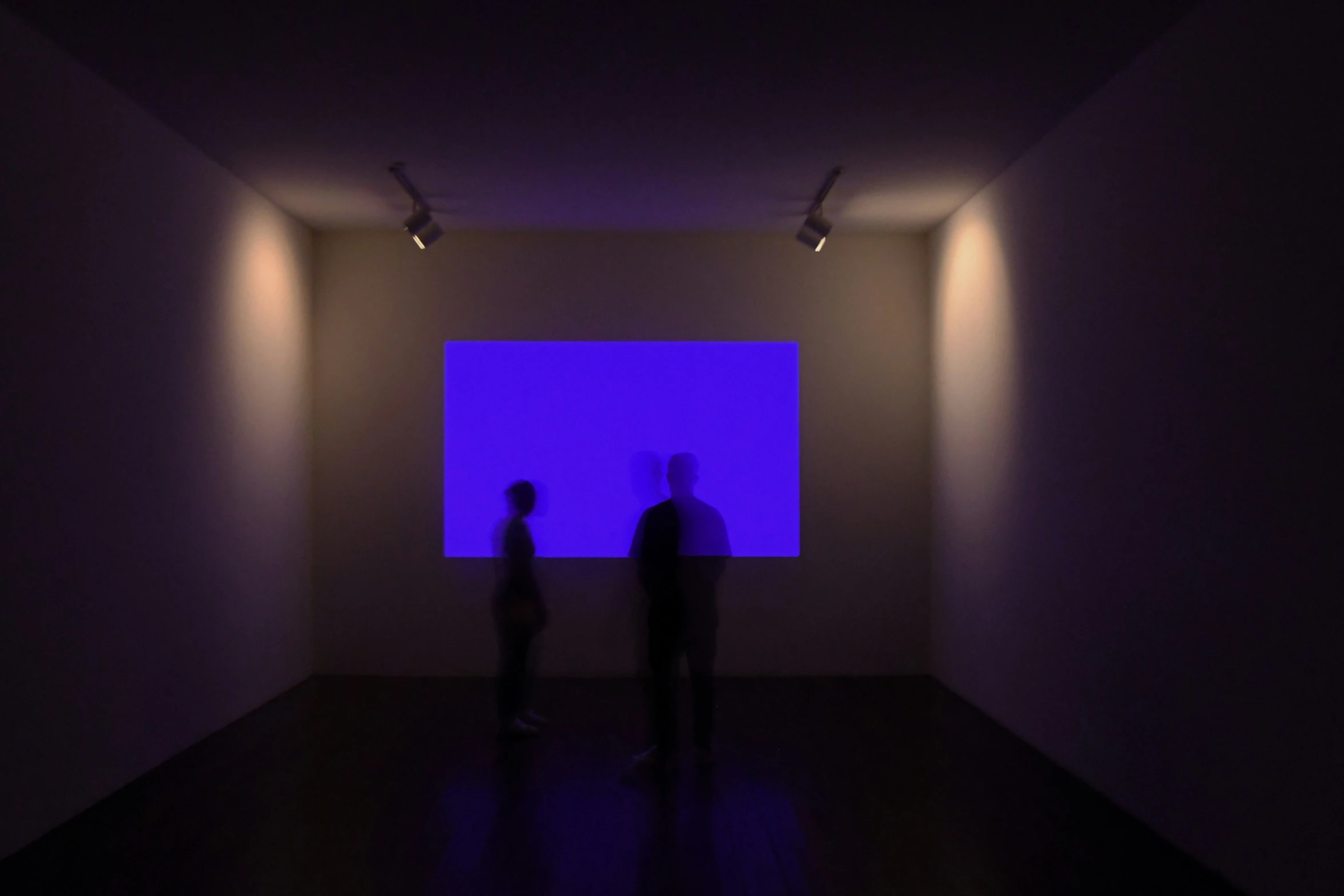 two people standing in an empty room with a blue screen