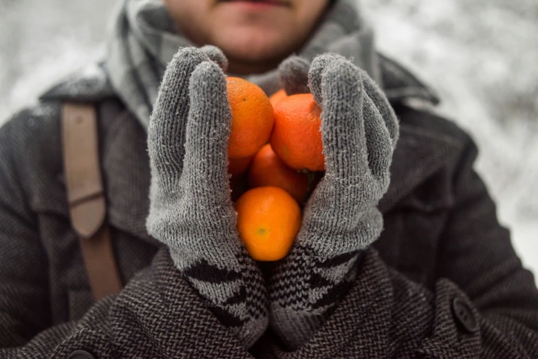 someone wearing gloves holding oranges in the snow