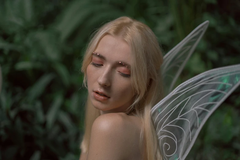a blond fairy with erfly wings looks at the camera