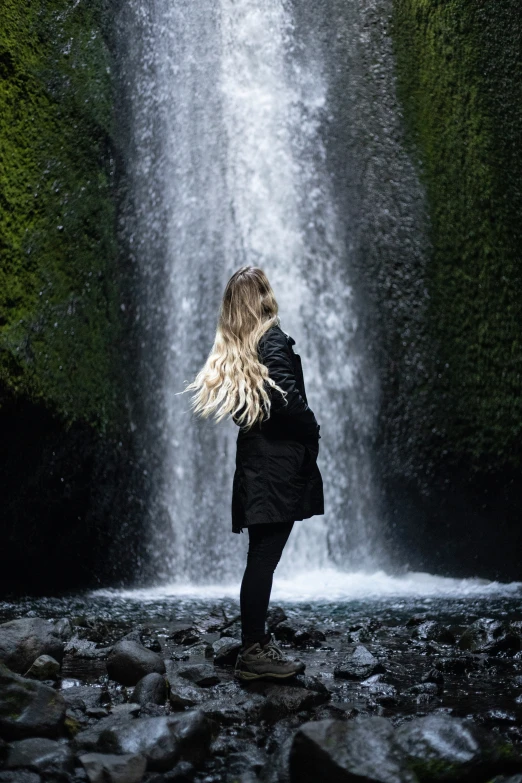 a woman looking up at a tall waterfall