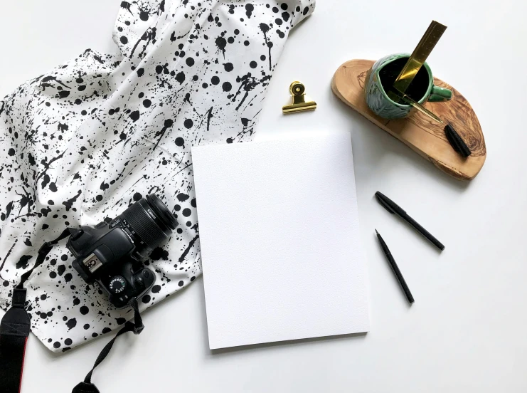 a pen, camera and notepad sit on a table