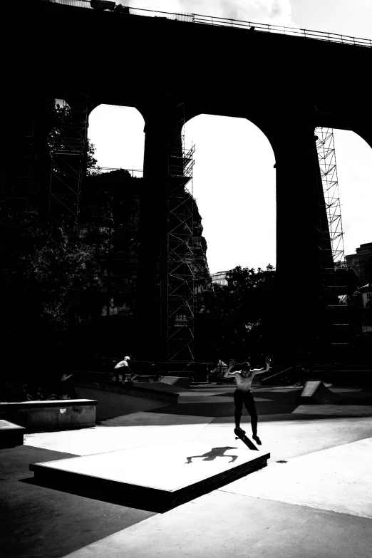 a person in the dark rides his skateboard near an arched walkway