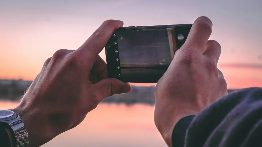 man's hand taking po with his phone on the beach at sunset