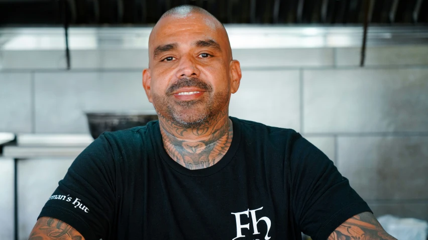 bald man with tattoos sitting down in front of table