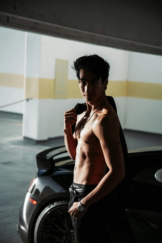 a shirtless man standing in front of a car