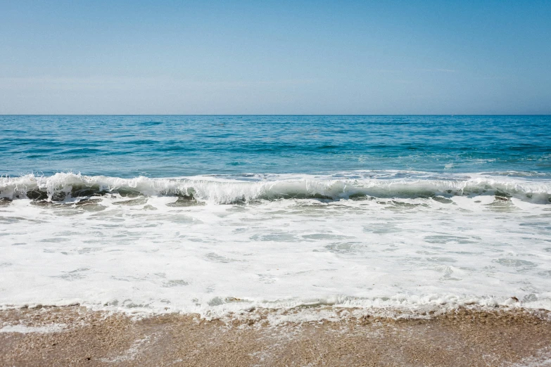 a blue sky, light green ocean, and a small wave on the beach