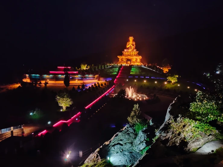 the view from the top of a hill with a bridge, lights and a large building