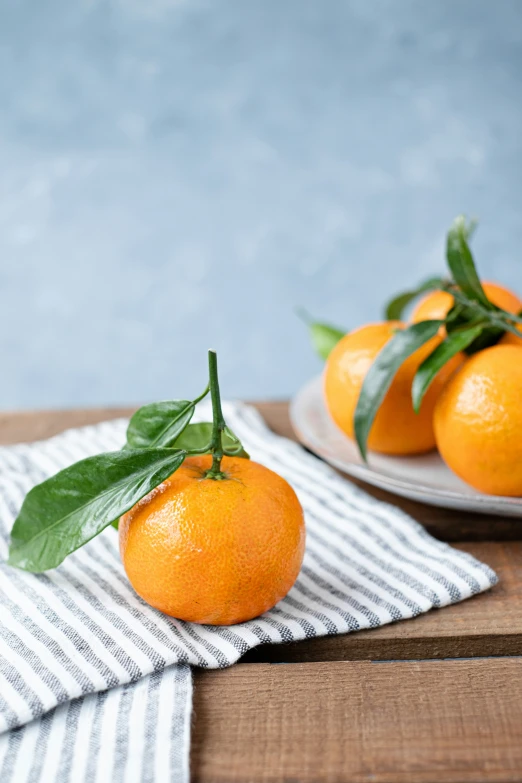 several oranges sit on a striped napkin on a table