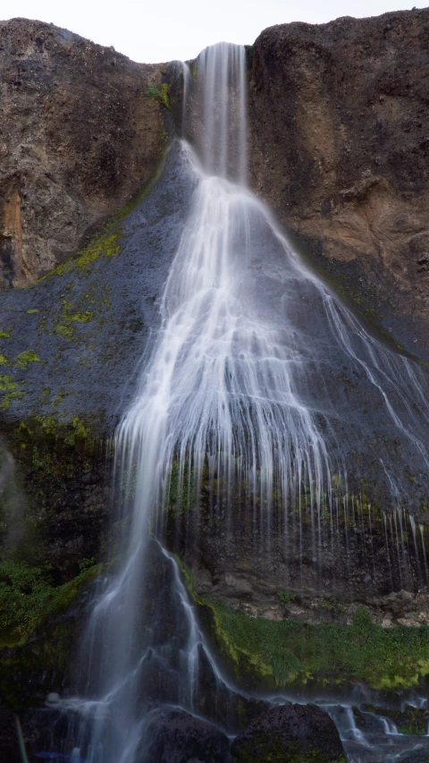 a close - up po of a waterfall with mossy plants growing out the side