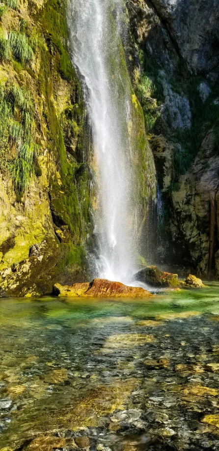 a waterfall surrounded by lots of moss on top of a cliff