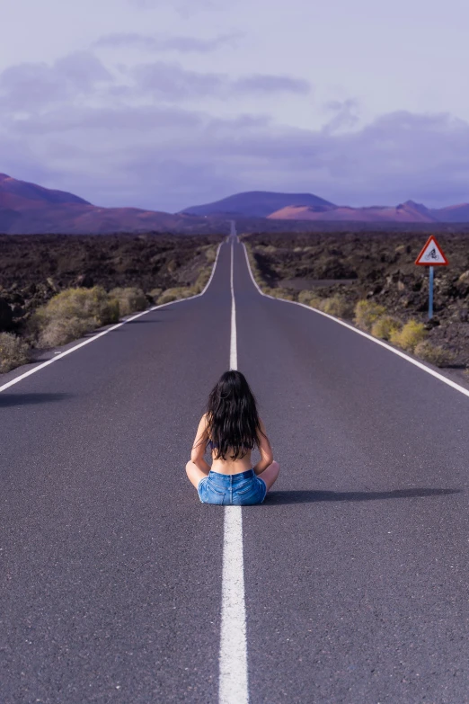 a woman sitting on the middle of an empty highway