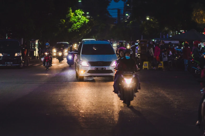 an illuminated night driving down a street with people riding motorcycles