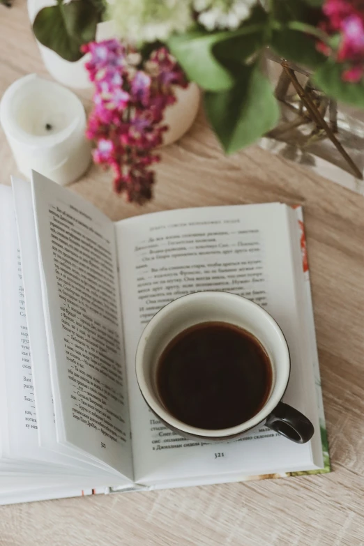 a cup of coffee on a table next to an open book