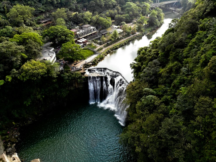 the top of a waterfall falls, above which is a road with lots of trees