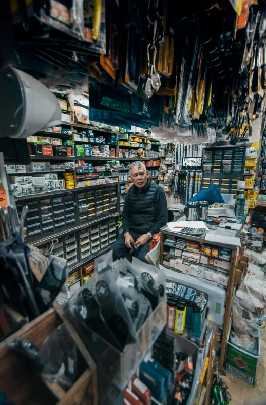 the shop owner is seated on his chair next to a rack of items