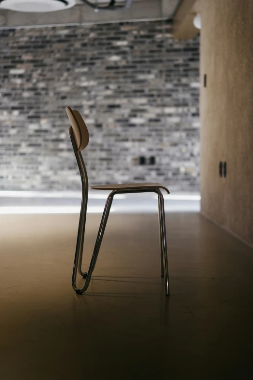 a metal chair on the floor in front of a brick wall