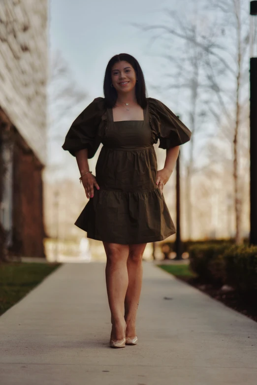 a woman with a white booties on, in a dark green dress, standing on the sidewalk