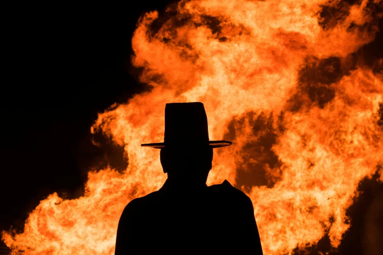 a man in a hat is silhouetted against a background of flames