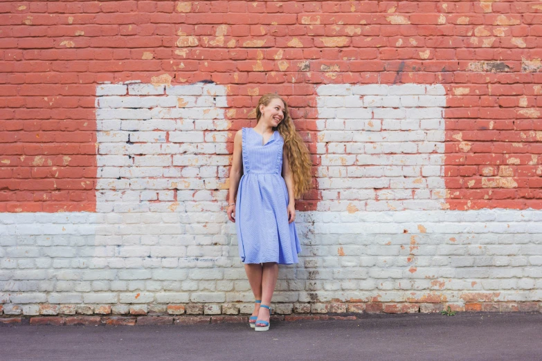 a woman leaning on a brick wall in a dress