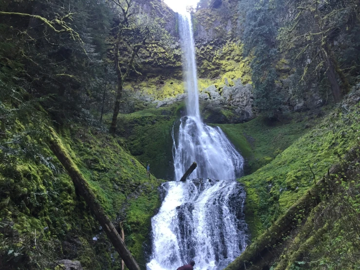 a waterfall with water and some vegetation in a hilly valley