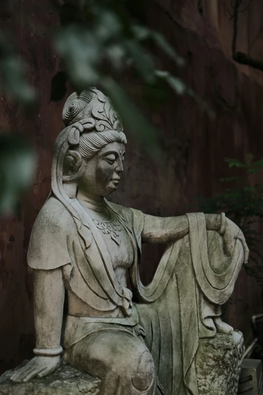 a statue sitting on top of a rock next to a tree