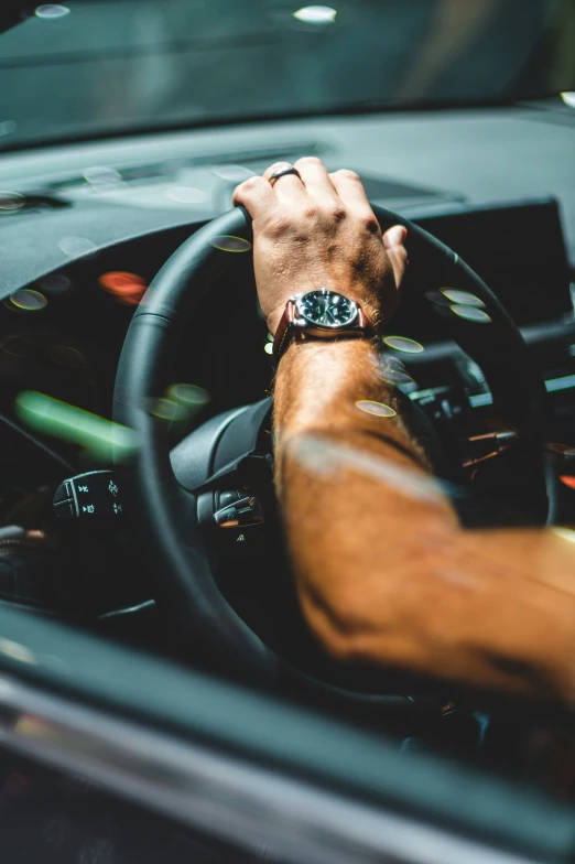 hands holding the steering wheel with both of them driving down a street