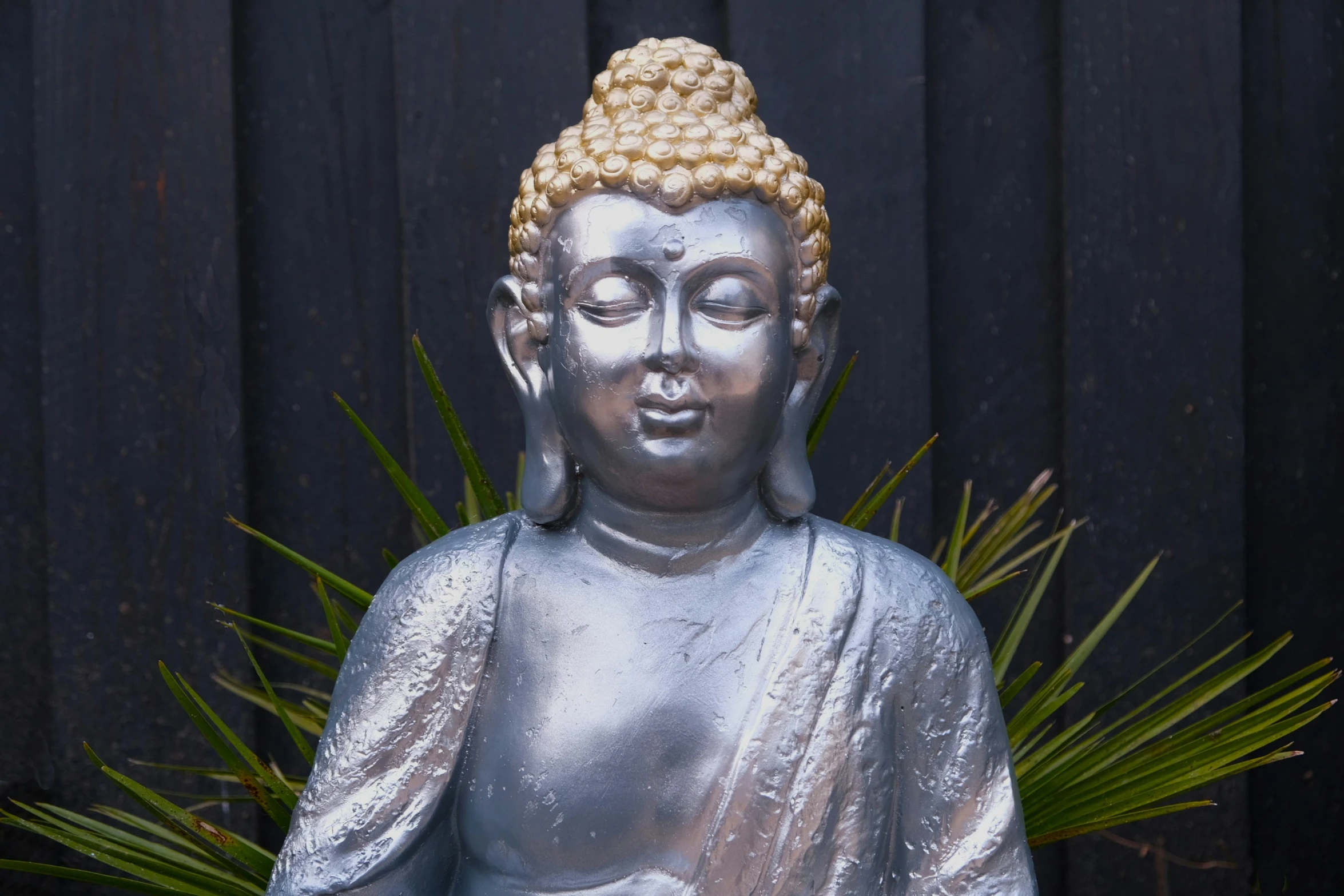 a silver statue of buddha with plants in the foreground