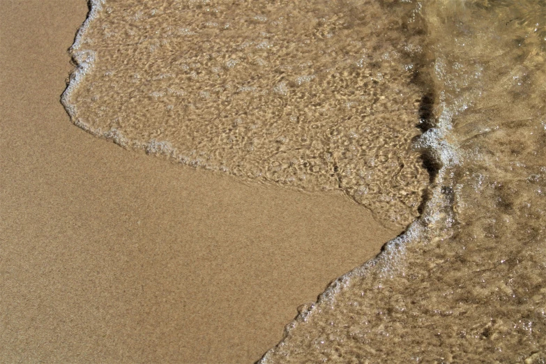 an ocean wave rolls over sand and foamy water