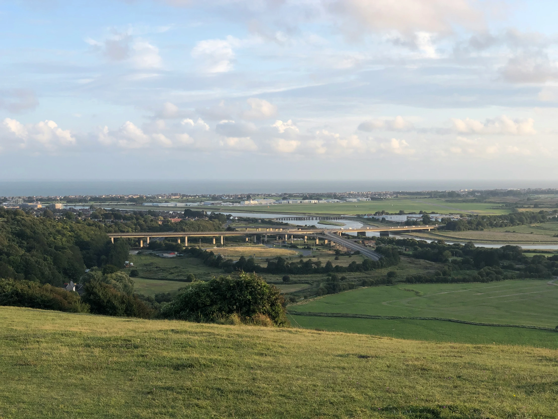 a view of some grass and hills with a bridge in the background