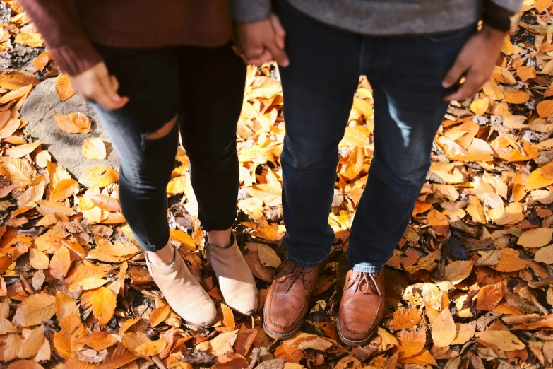 two people holding hands and standing among fallen leaves