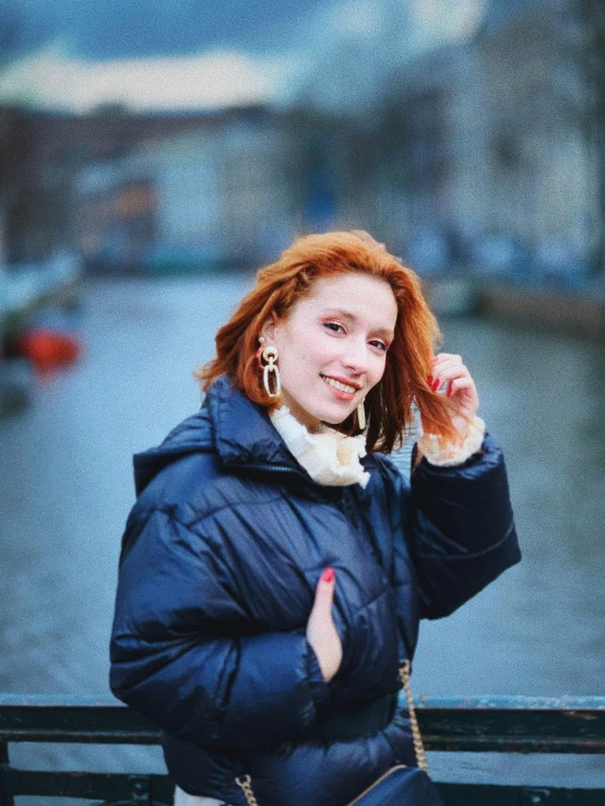 a woman poses by the water and wears a coat