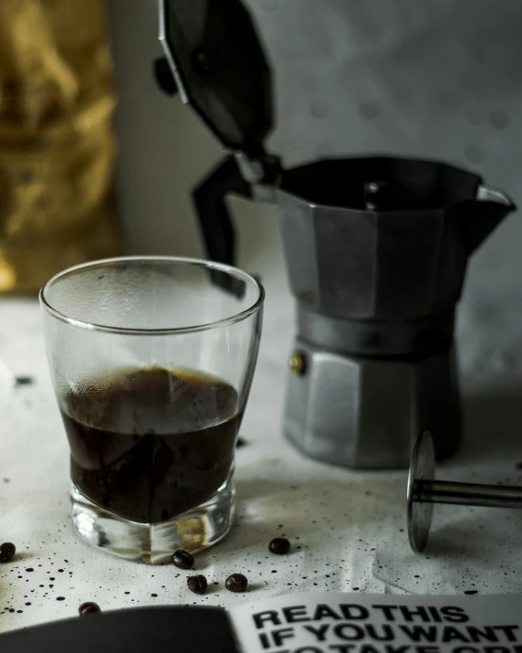 a glass of drink sitting on a table next to a blender and an aluminum tea pot