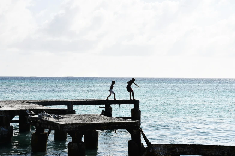 people are walking on a wooden pier over the ocean