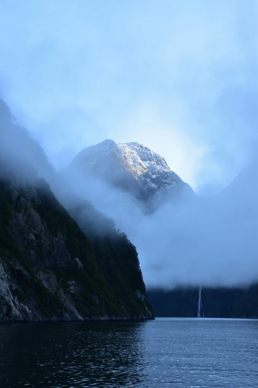 mountain range in front of water with clouds coming out