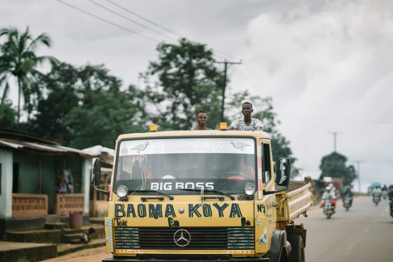 three people ride on the back of a yellow truck