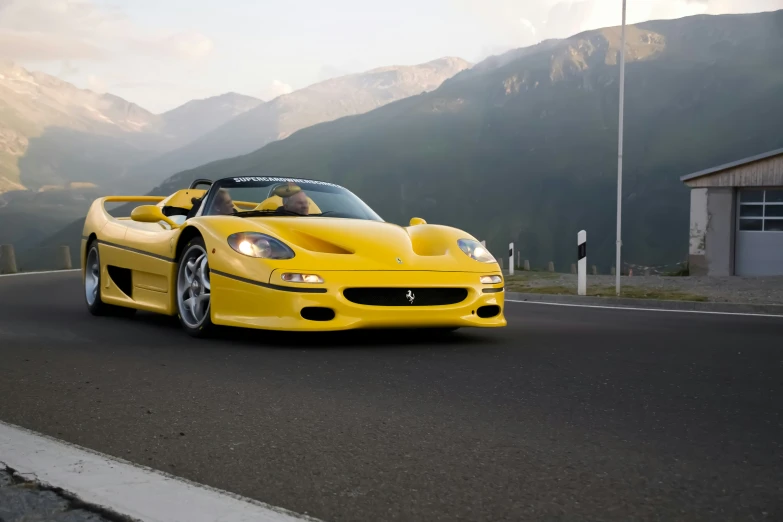 a yellow car driving down a road next to mountains