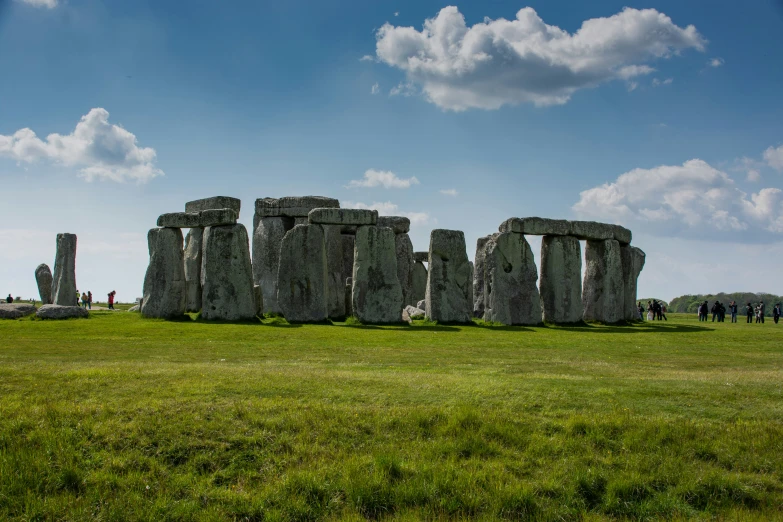 a couple of stonehenge in the grass with blue skies in the background