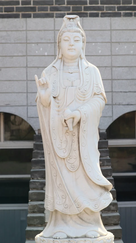 white statue standing outside of a building with its hand on the ground