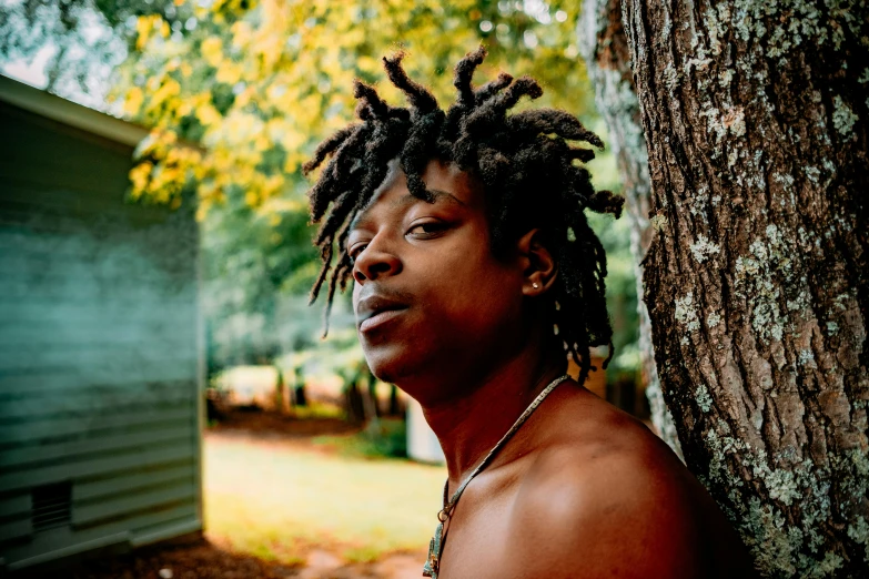 a black man with dreadlocks is standing next to a tree