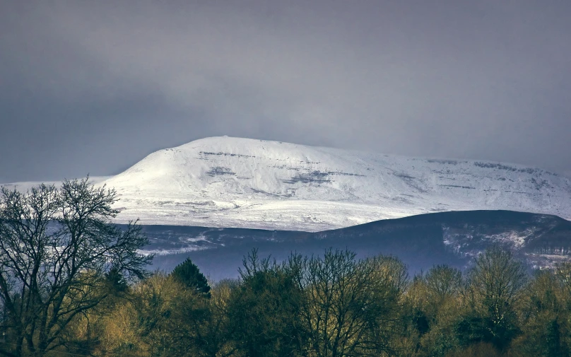 a mountain covered in snow sitting next to trees