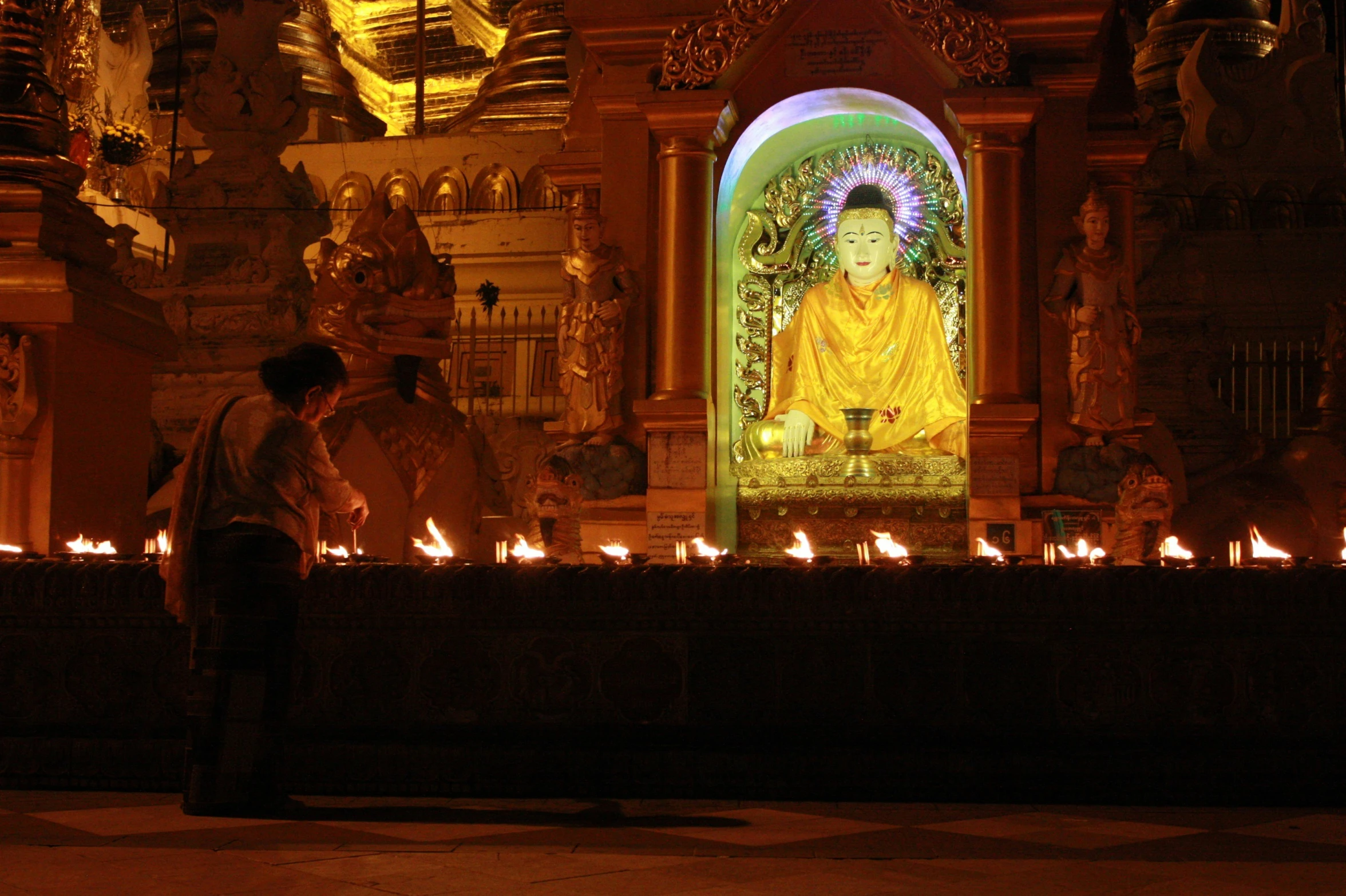 two people standing in front of a lit up buddha