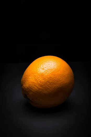 an orange sitting on the ground near a black background