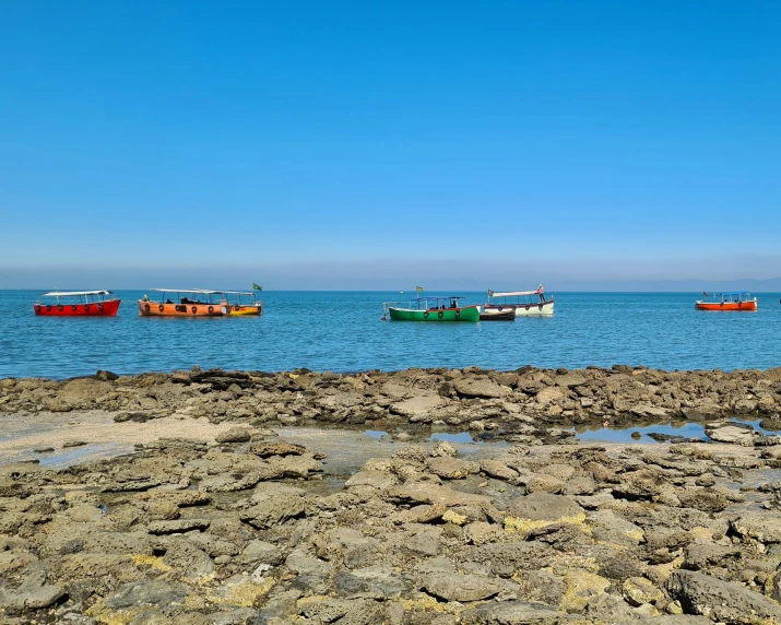 several colorful boats out in the ocean near a sandy shore