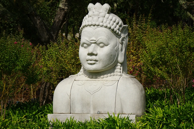 a statue is pictured among the greenery in the foreground