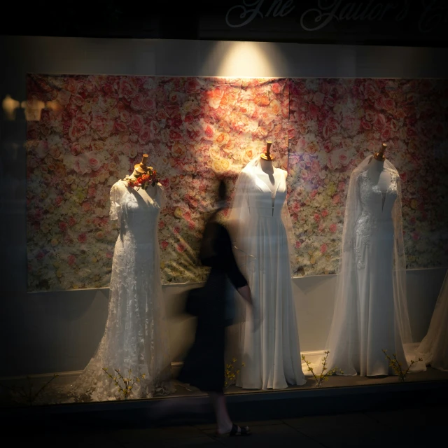 a woman walks past dresses in a window display