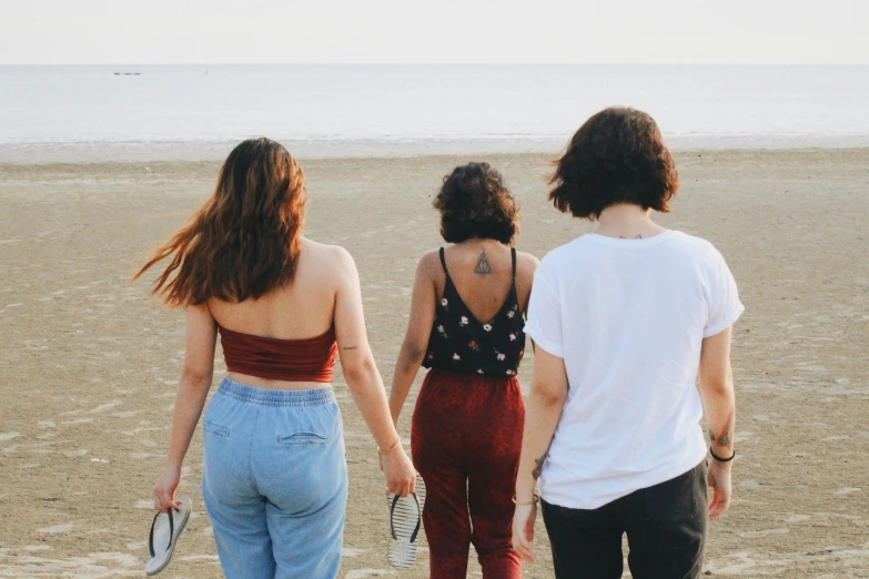 a couple of women walking down a beach with people watching