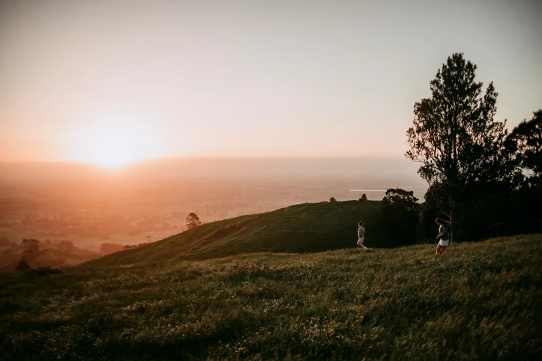 the couple stand at the top of a grassy hill with a view of the city and trees in the background