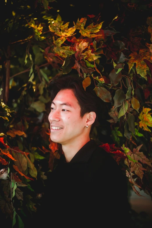 an asian man smiling and surrounded by leaves