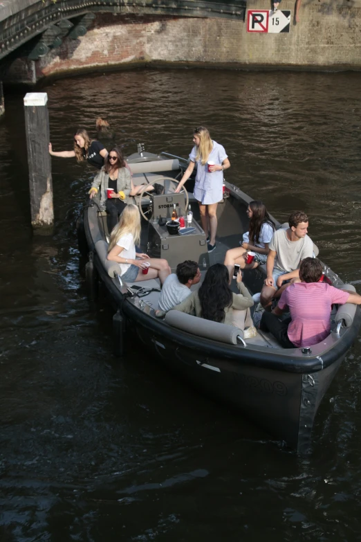 there is a man driving a boat as people are hanging out on the bridge