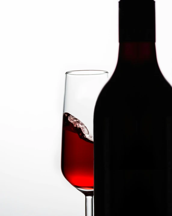 there is a red wine glass next to a wine bottle